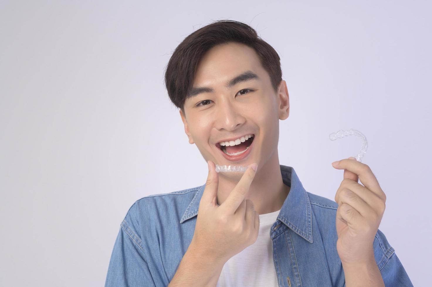 Young smiling man holding invisalign braces over white background studio, dental healthcare and Orthodontic concept. photo