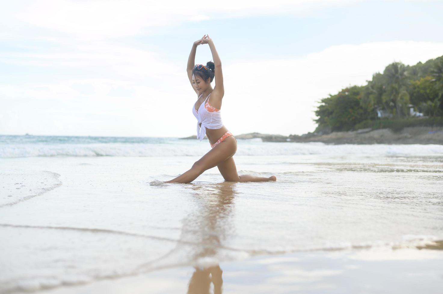 Young asian woman in bikini doing yoga on the beach, health and meditation concept photo