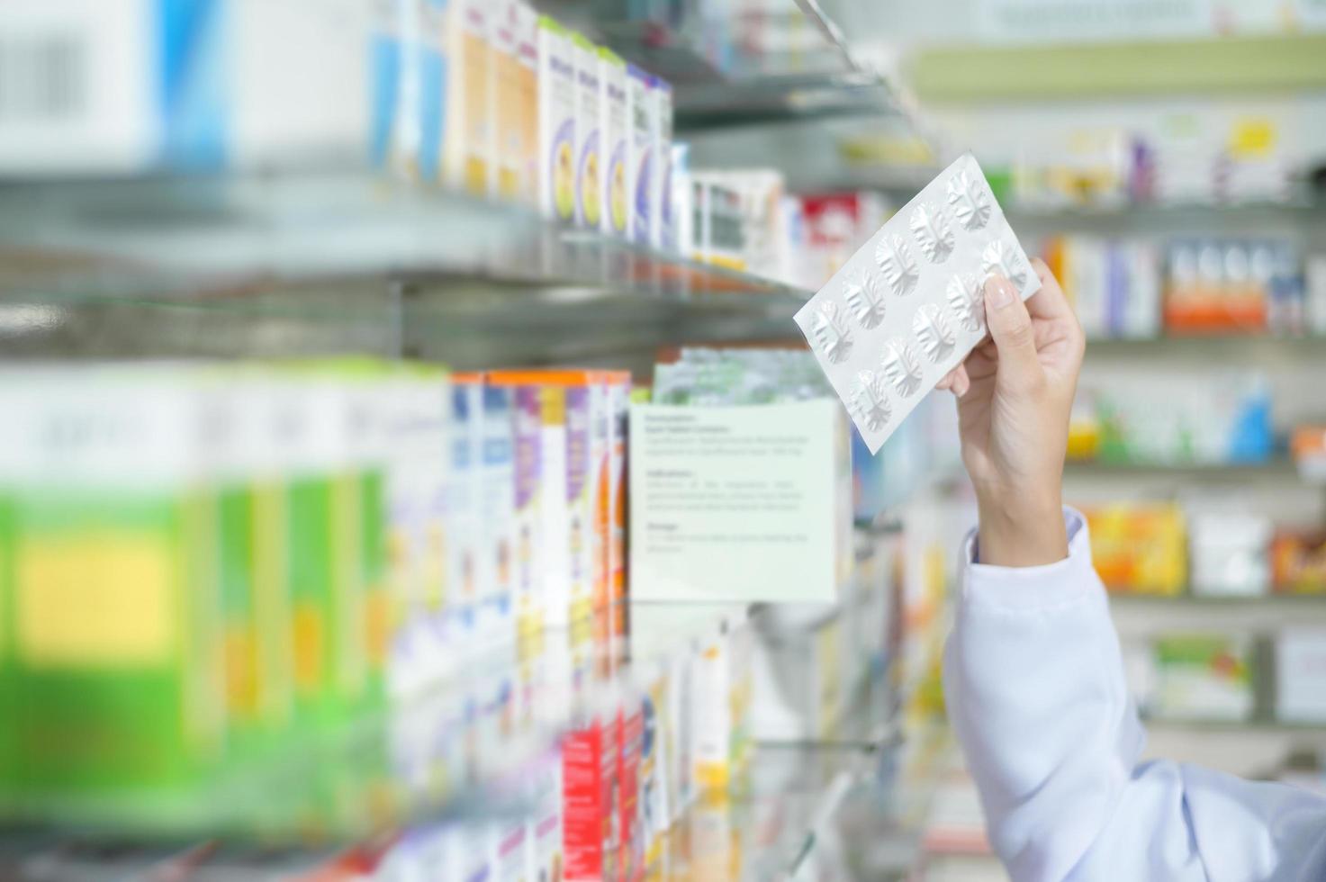 Farmacéutica con bata de laboratorio en una farmacia moderna, seleccionando un medicamento para el cliente. foto