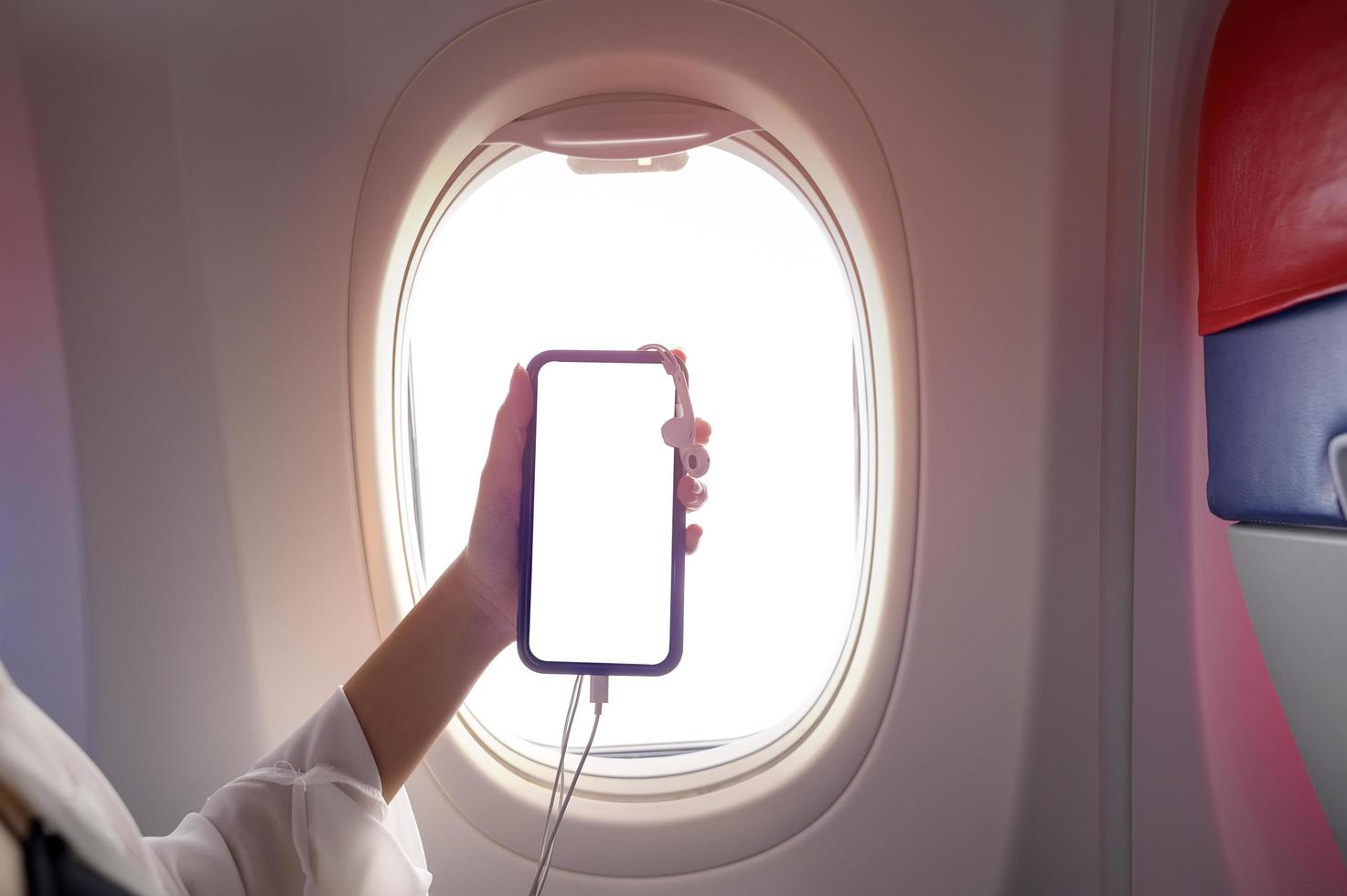Close up woman hand holding smartphone over window aircraft background , transportation technology concept photo
