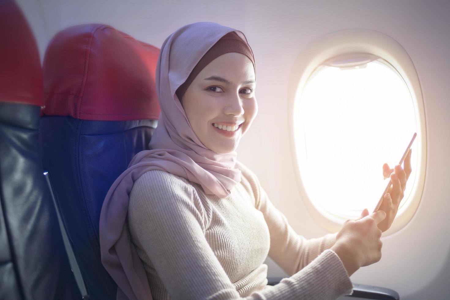 Young muslim woman wearing hijab using smartphone onboard, travel and holidays concept photo