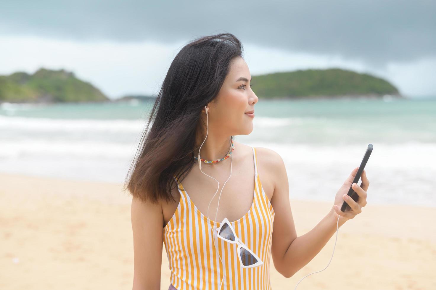 joven mujer hermosa en bikini escuchando música y usando un smartphone en la playa, verano, vacaciones, vacaciones, concepto de estilo de vida. foto