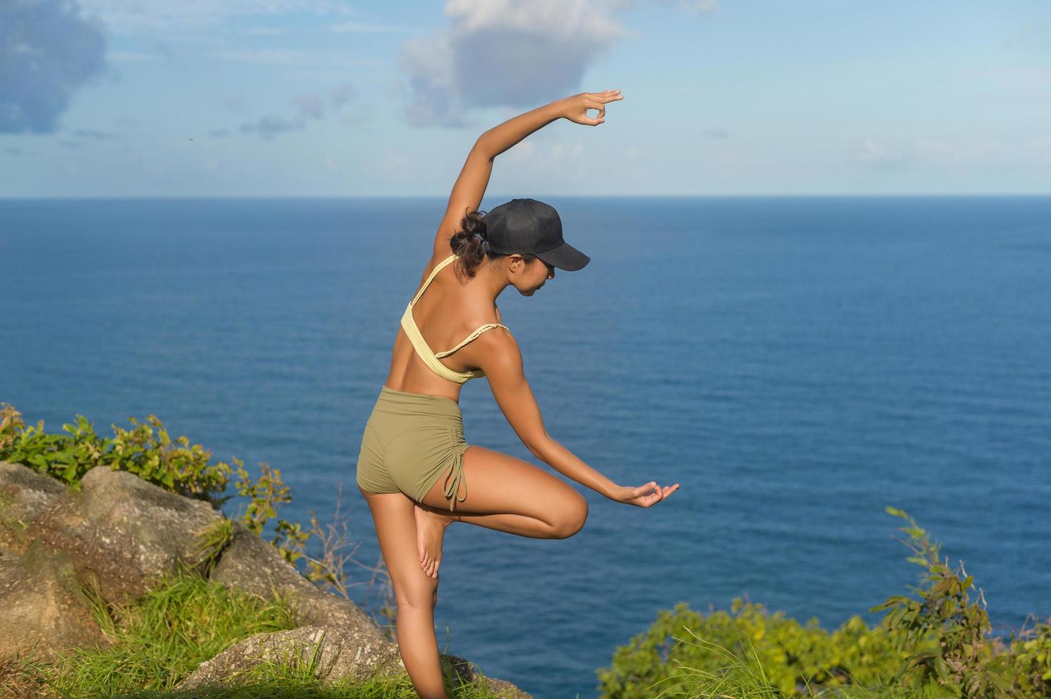 Beautiful asian woman in sportswear doing yoga on seaside mountain peak after trekking, Travel and meditation concept. photo