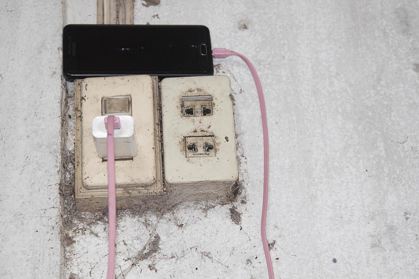 Power sockets and charging cables for phones and phones are essential technology these days, with cobwebs on the cement floor. The walls of the house look dirty and lack maintenance. photo