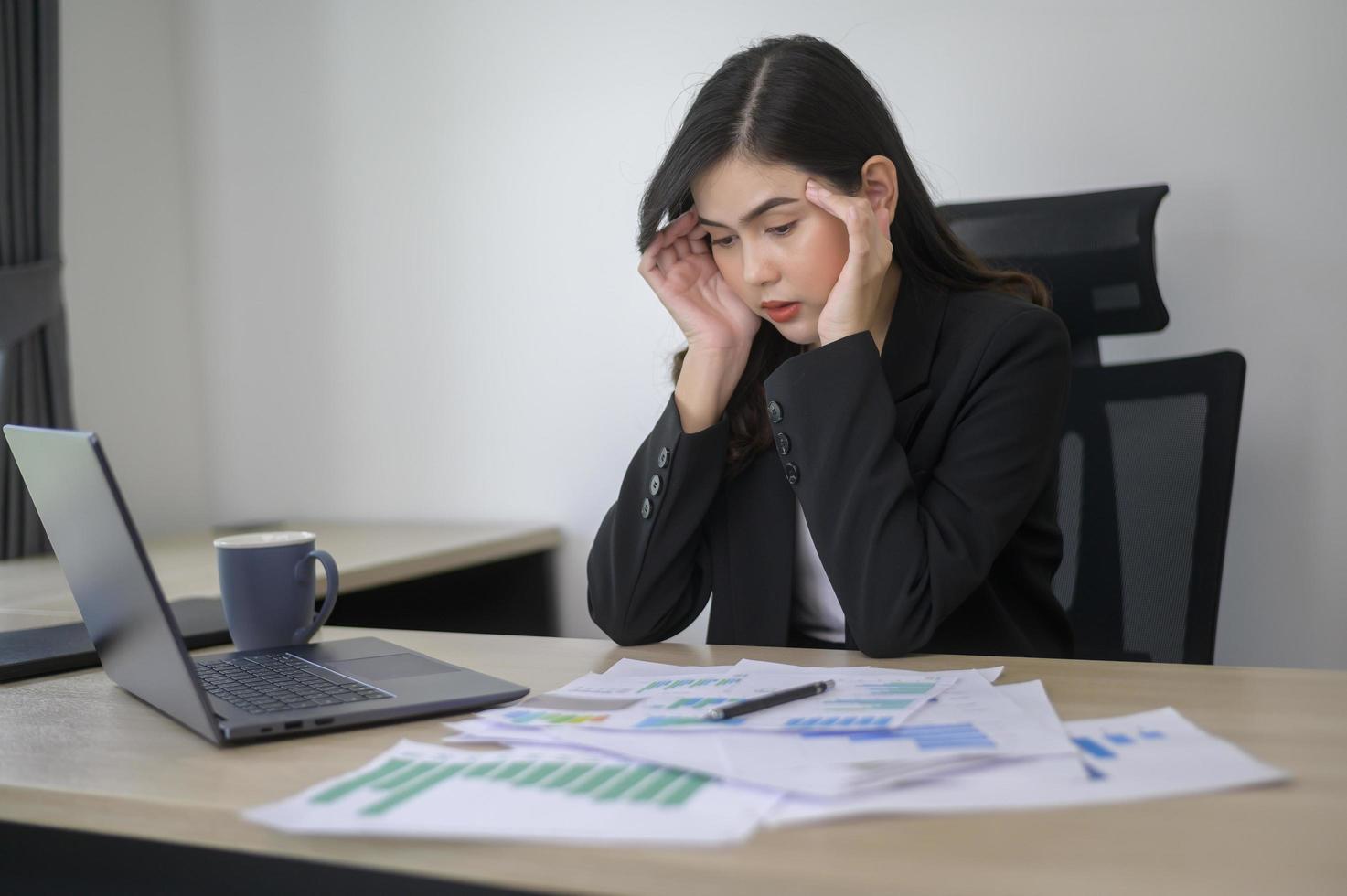 Stressed young business woman working on laptop with documents in modern office, workload concept photo