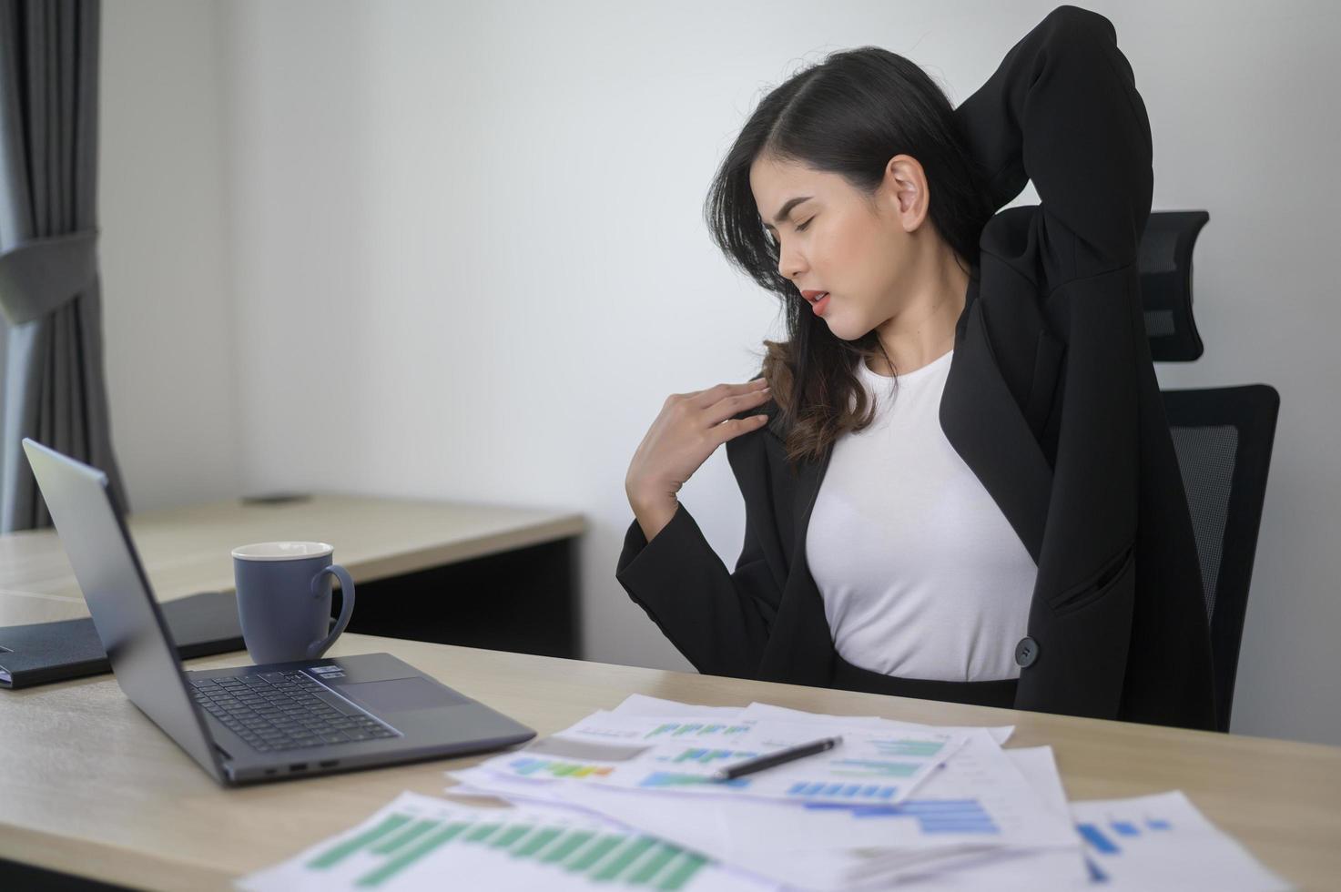 Stressed young business woman working on laptop with documents in modern office, workload concept photo