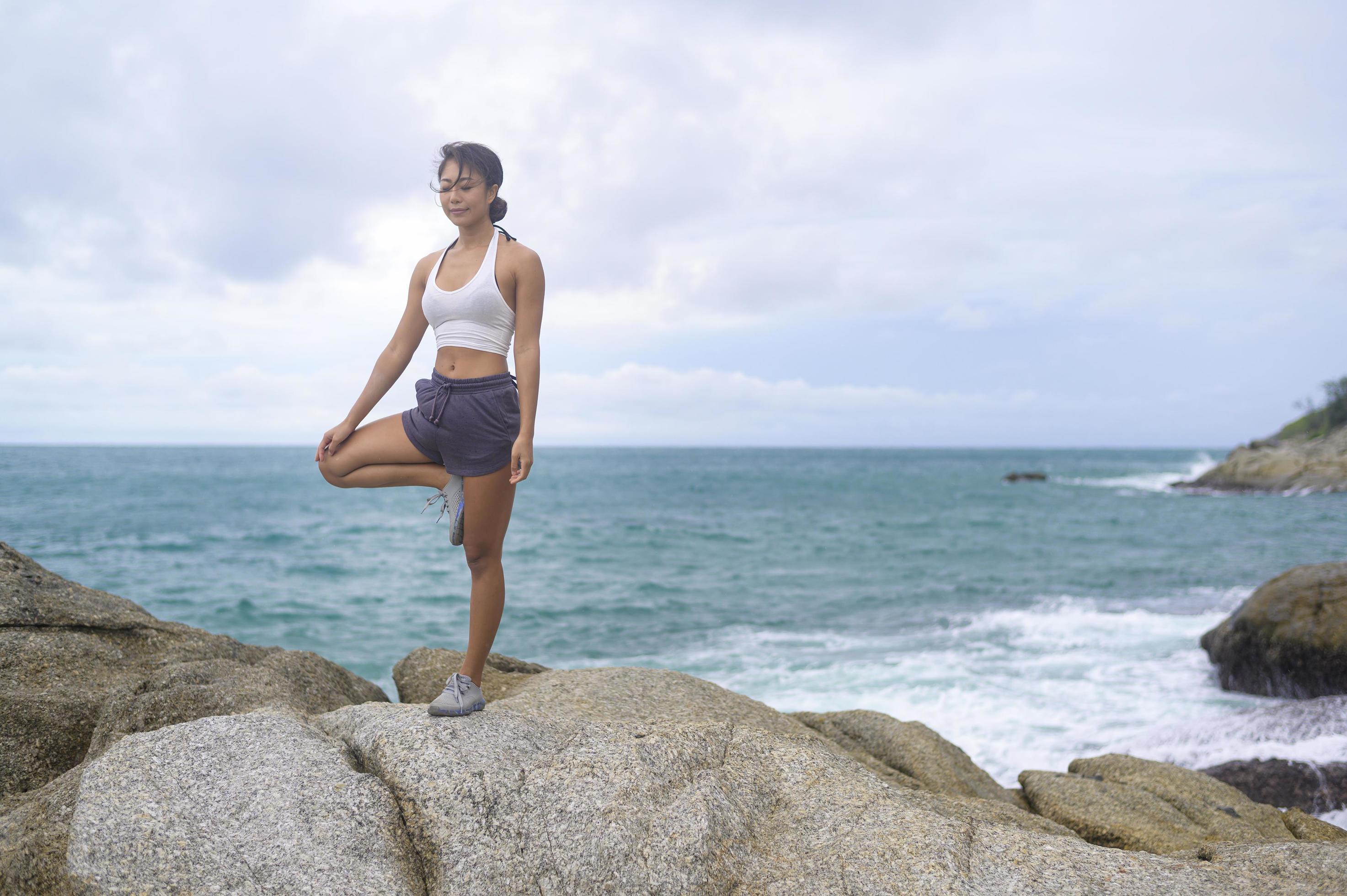 Young asian woman in sportswear doing yoga on the rock at seaside, health  and meditation concept 9285278 Stock Photo at Vecteezy