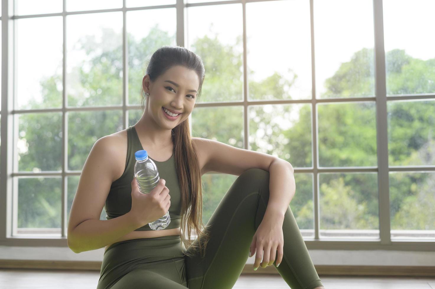 mujer joven fitness en ropa deportiva bebiendo agua después de hacer ejercicio en casa, saludable y estilos de vida. foto