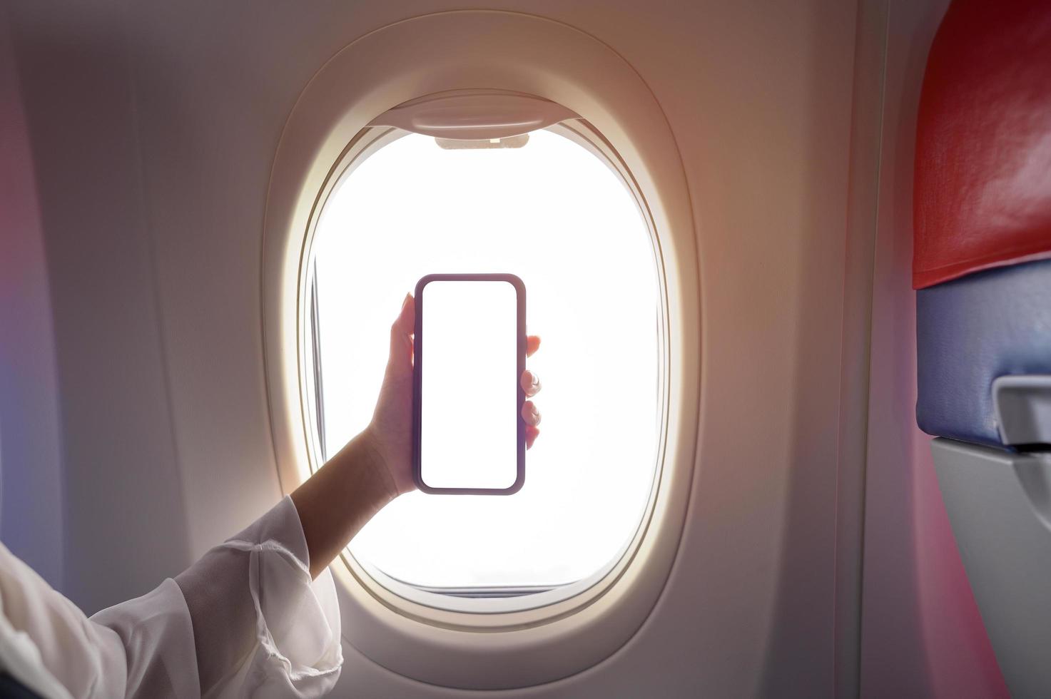 Close up woman hand holding smartphone over window aircraft background , transportation technology concept photo