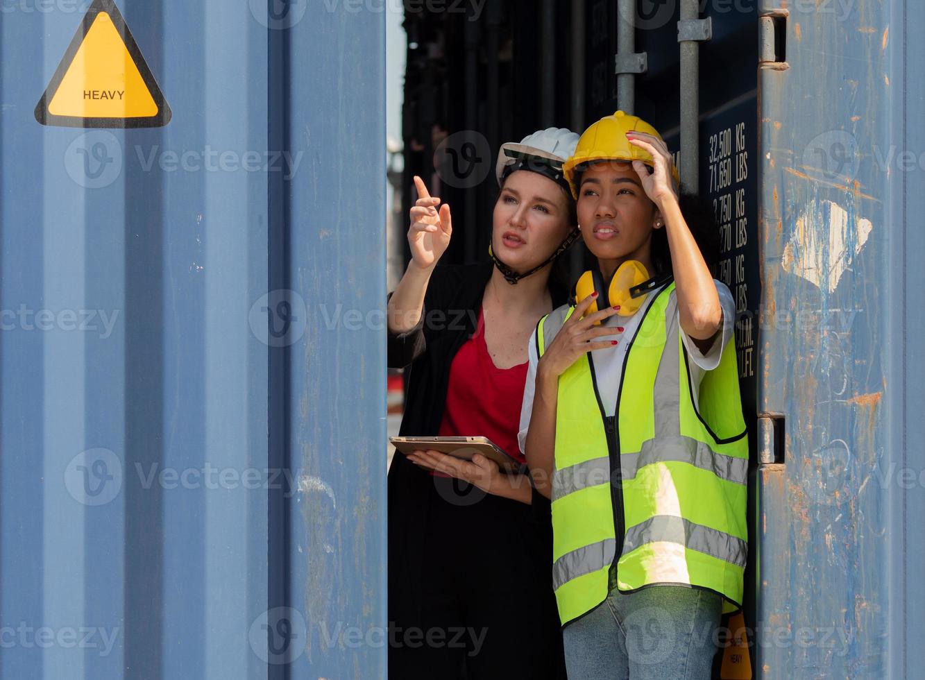 African American female foreman and colleague watching cargo loading boxes at container yard, portrait. Diverse engineer women work at shipping dockyard, a multicultural workplace. Diversity concept. photo