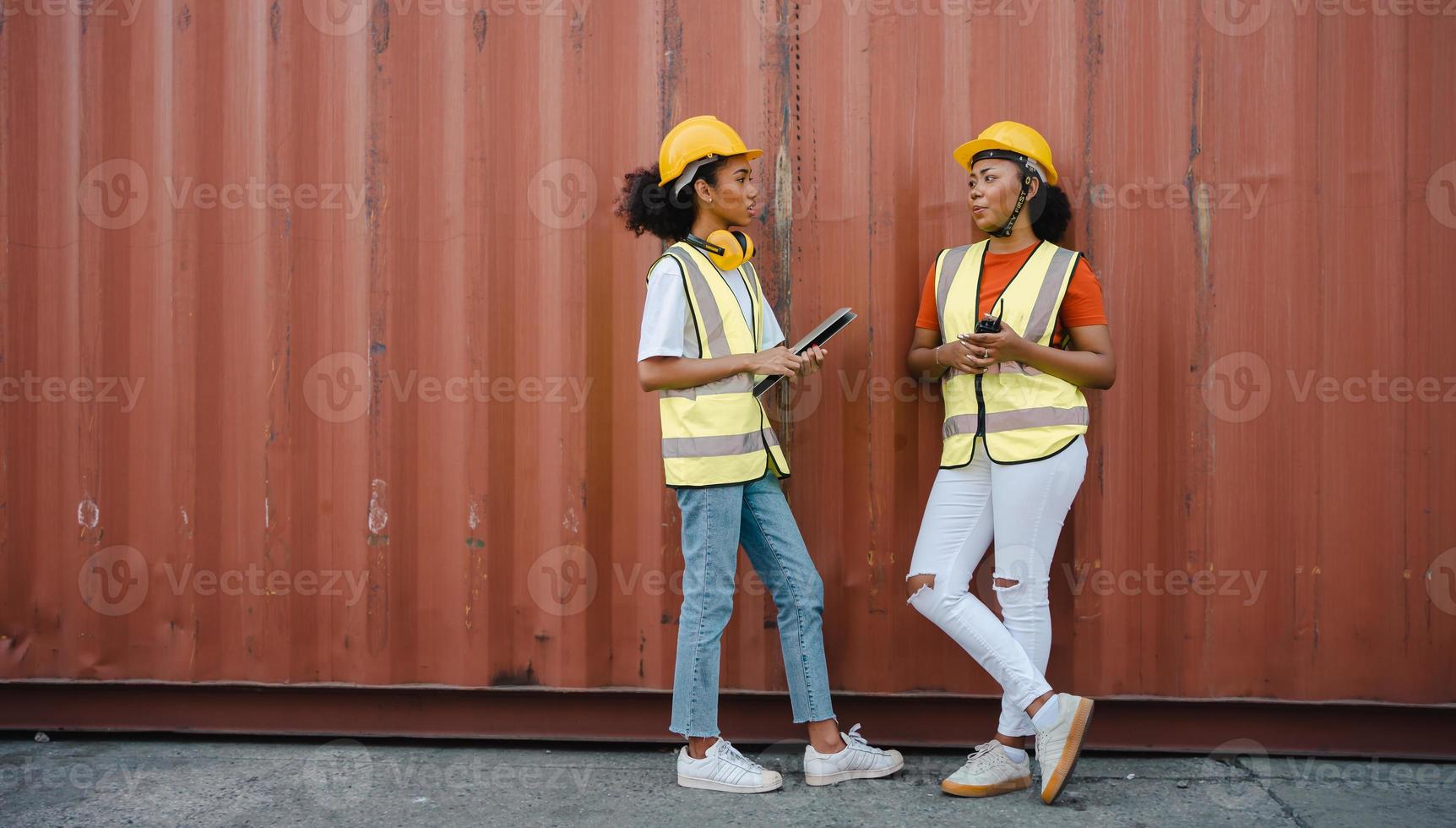 Two female foreman workers work at the container yards. African American women, industrial engineers with laptop and walkie talkie working at international logistics cargo terminal. Two people talking photo