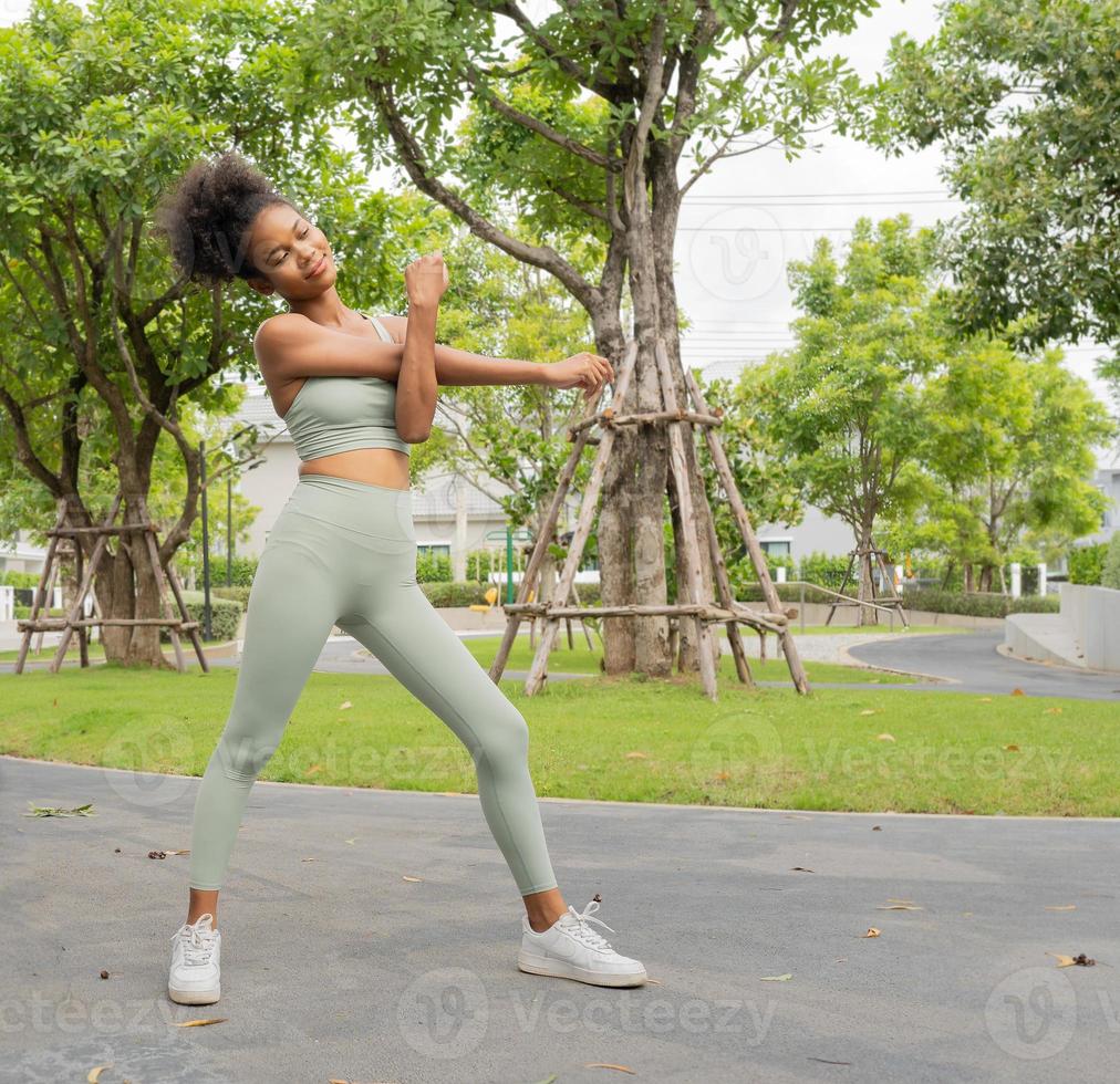 joven negra estirando, haciendo ejercicio en el parque natural. hermosa  chica en ropa deportiva calentándose con
