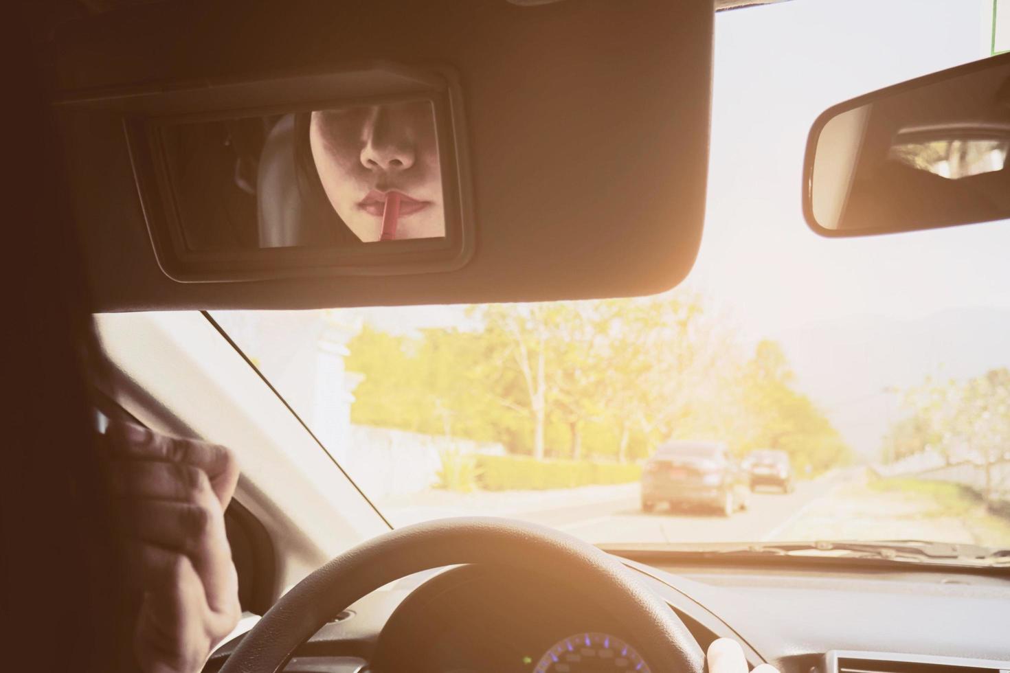 Woman making up her face using lipstick while driving car, unsafe behavior photo