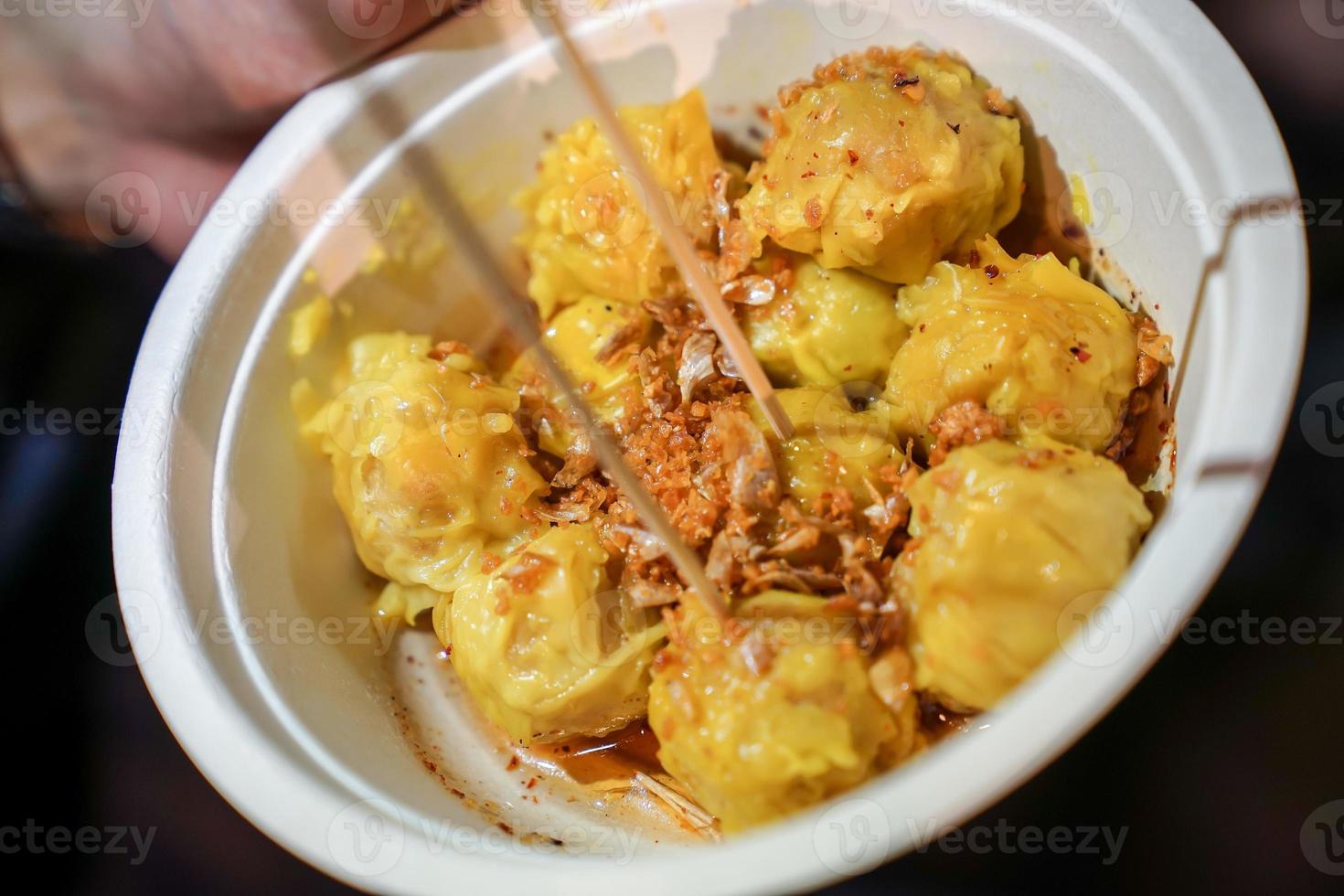 A yellow steamed dumpling topping with fried garlic put in the paper cup. At Bangkok Thailand foodstruck streetfood. photo