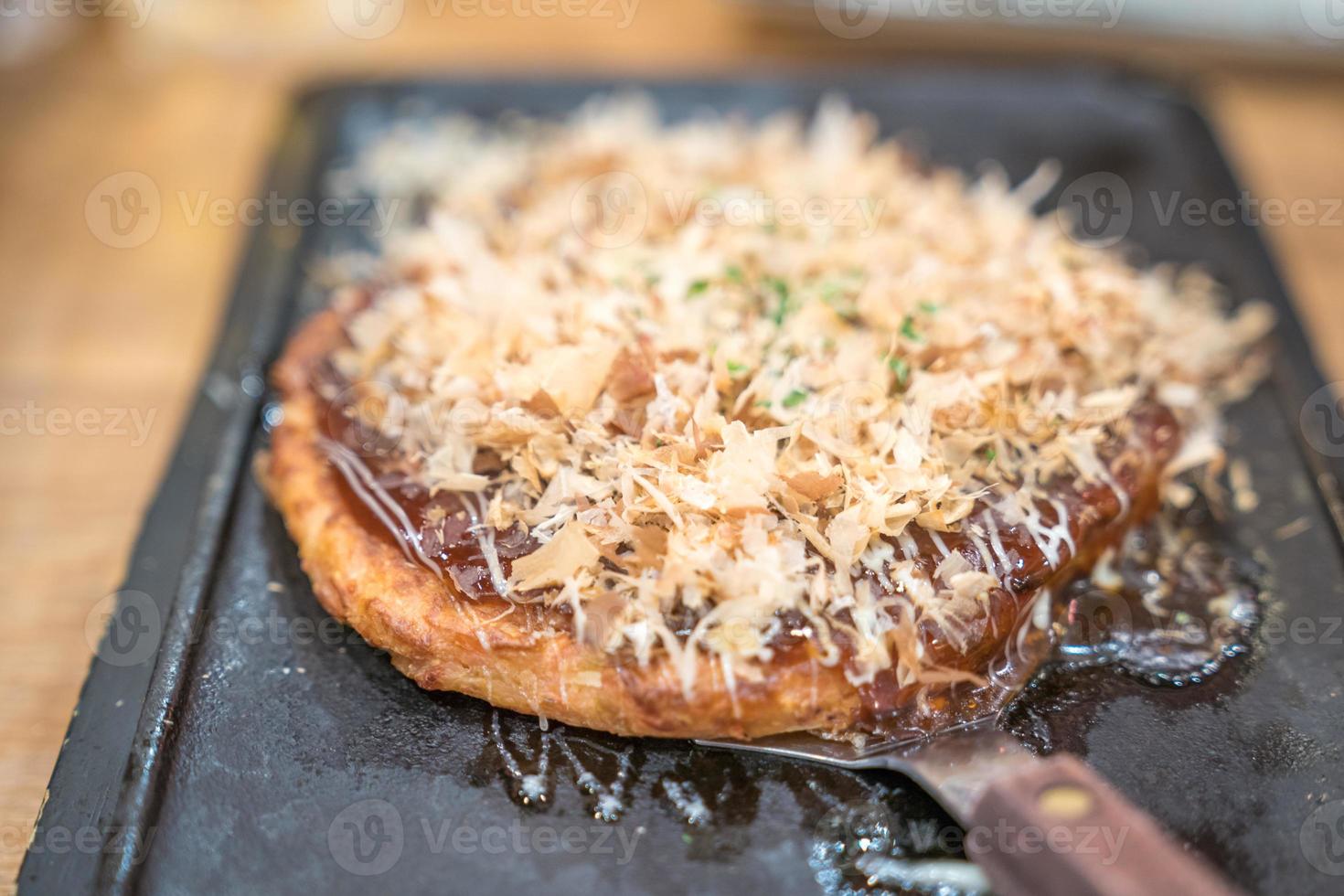 okonomiyaki tranditional Japanese food style handmade and cut on a iron plate ready to serve and eat at a restaurant. close up shot. photo