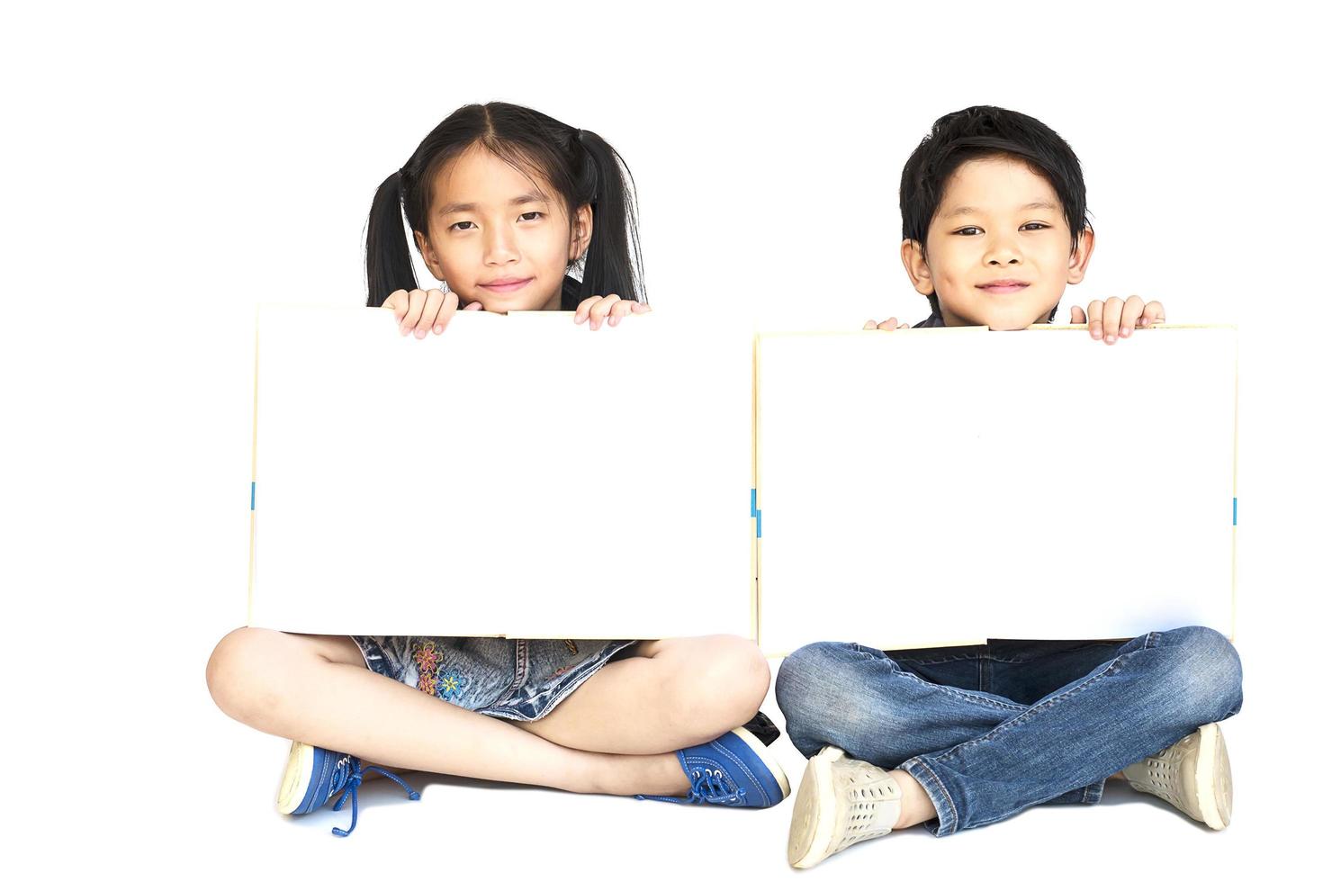 Niña y niño de la escuela asiática de 10 y 7 años mostrando felizmente un libro blanco vacío aislado en blanco foto