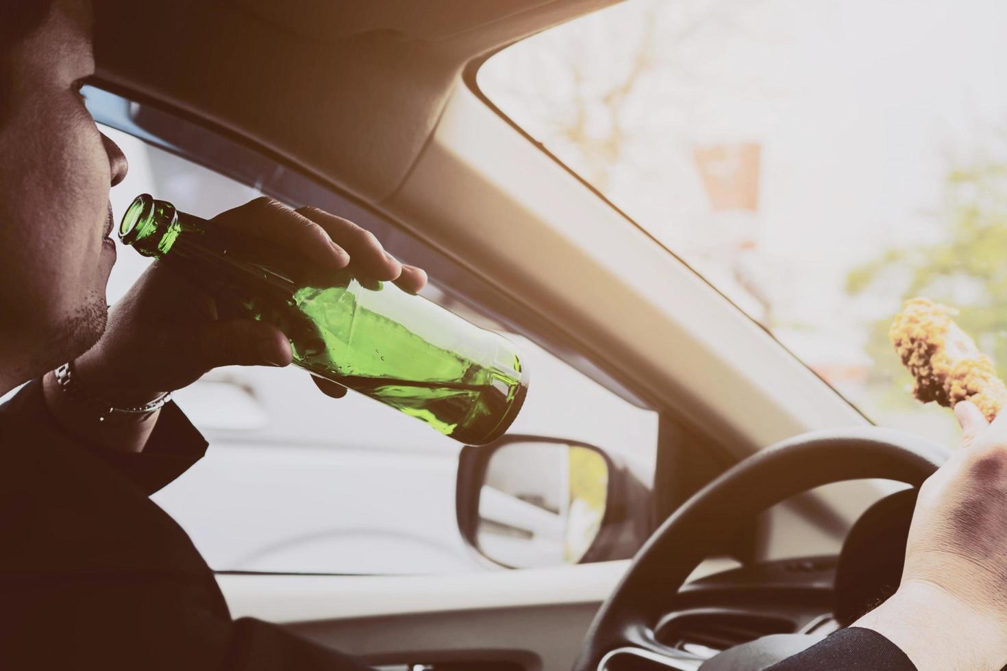 Man drinking beer and eating fried chicken while driving a car photo