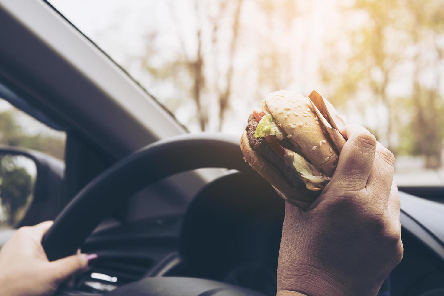 señora conduciendo un coche mientras come una hamburguesa foto