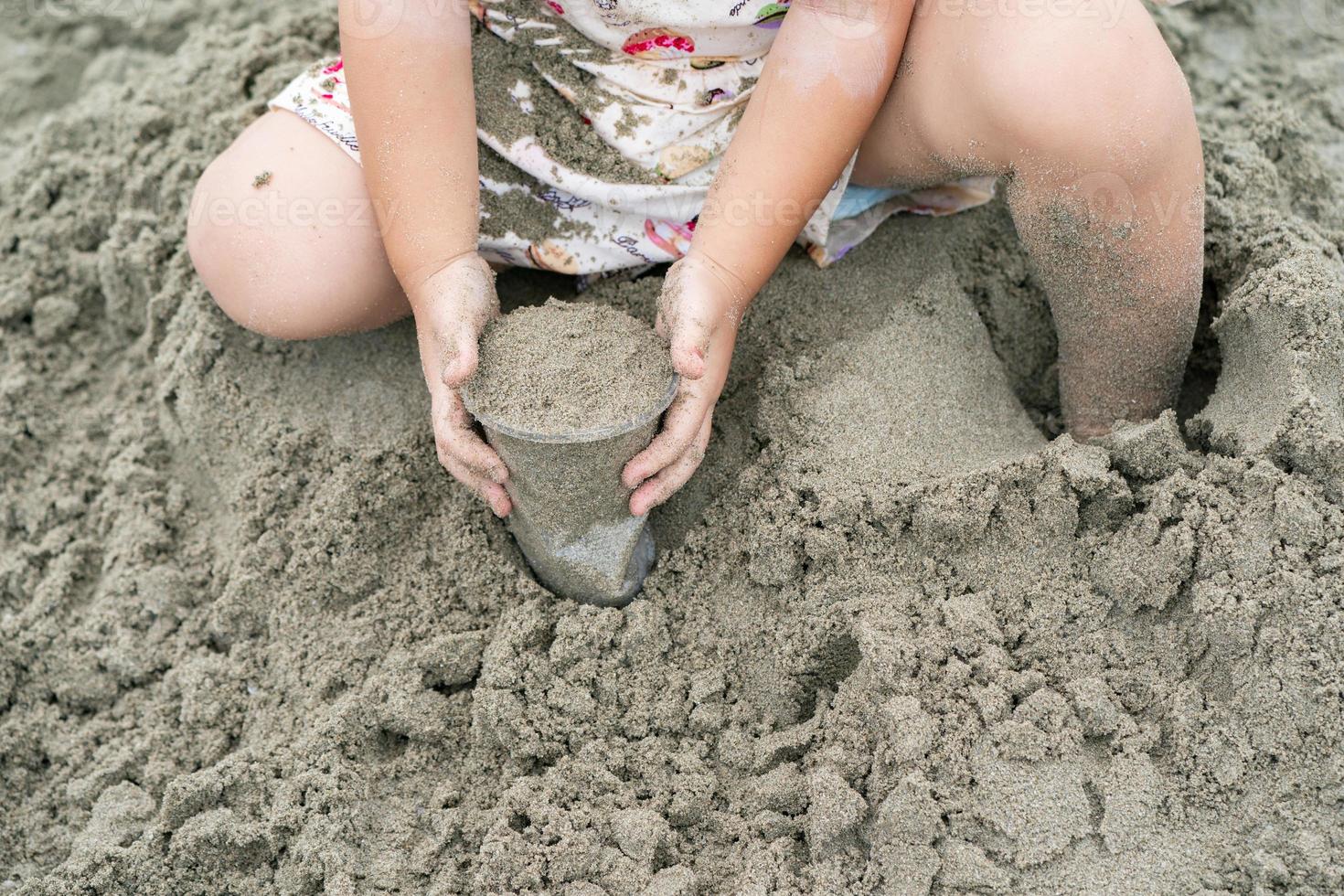 Kid holds and plays sand in the plastic cup on the beach. photo