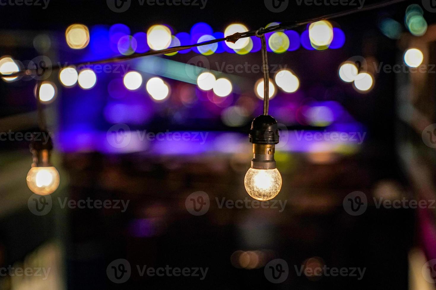 concéntrese en la lámpara colgante de círculo vintage en la línea con un concierto al aire libre borroso en el fondo del bokeh nocturno. foto
