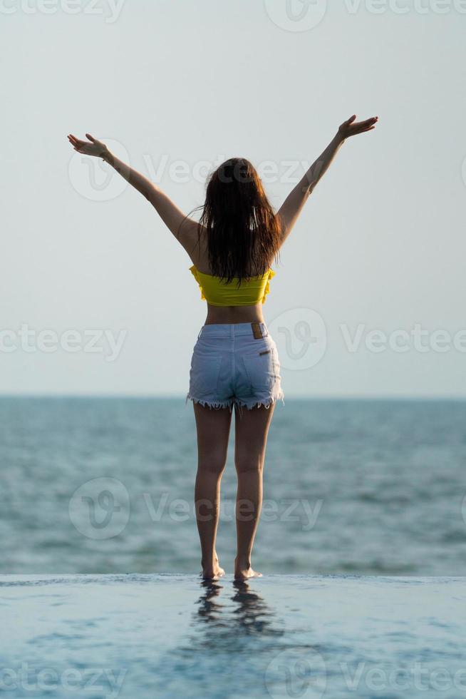 Asian Thai teenager female in Yellow relax and swim suit is posting on the infinity pool beside the sea beach in Thailand resort. photo