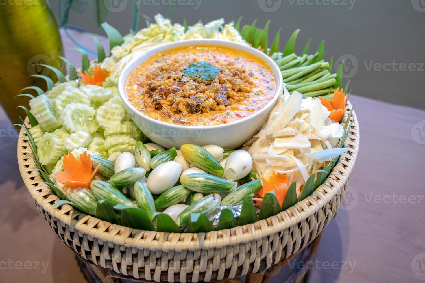 Traditional Thai chilli spicy sauce called Nam Prik in white bowl in the middle of vegetable cabbage cucumber carrot eggplant lentils ginger. photo