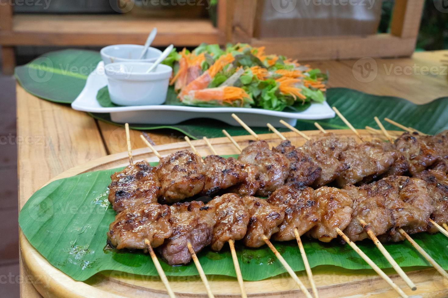 cooked grilled roasted pork sticks are arranged on the banana leaf and decoration food around this snack area for a seminar breaking time at outside garden. photo