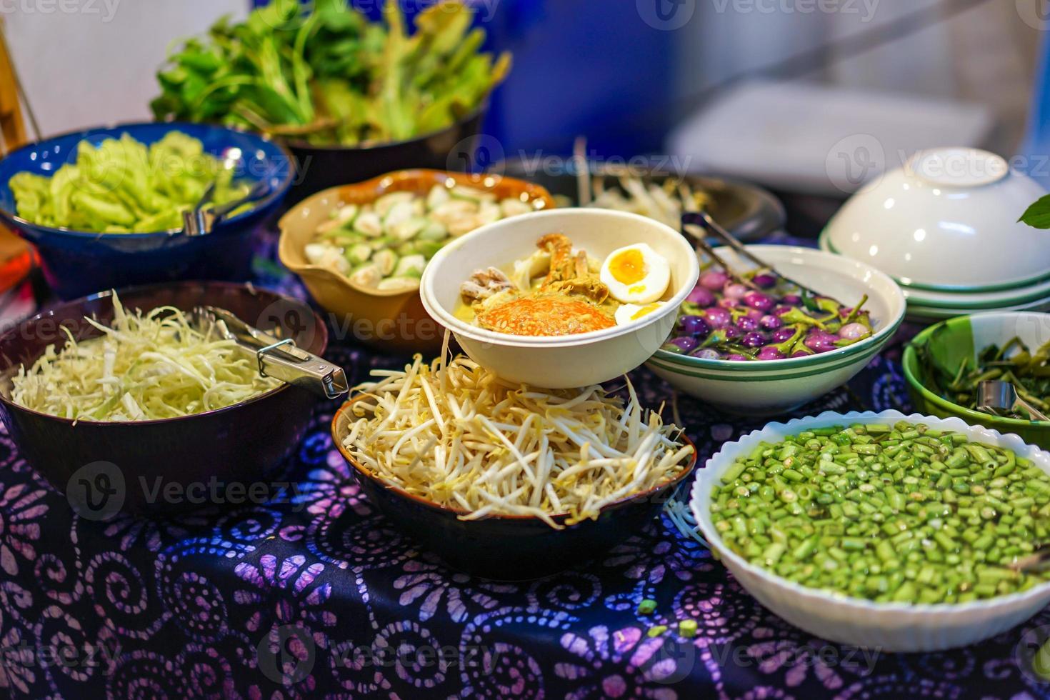 Traditional Thai spicy curry soup with noodle and crab on the table with vegetable around it. photo