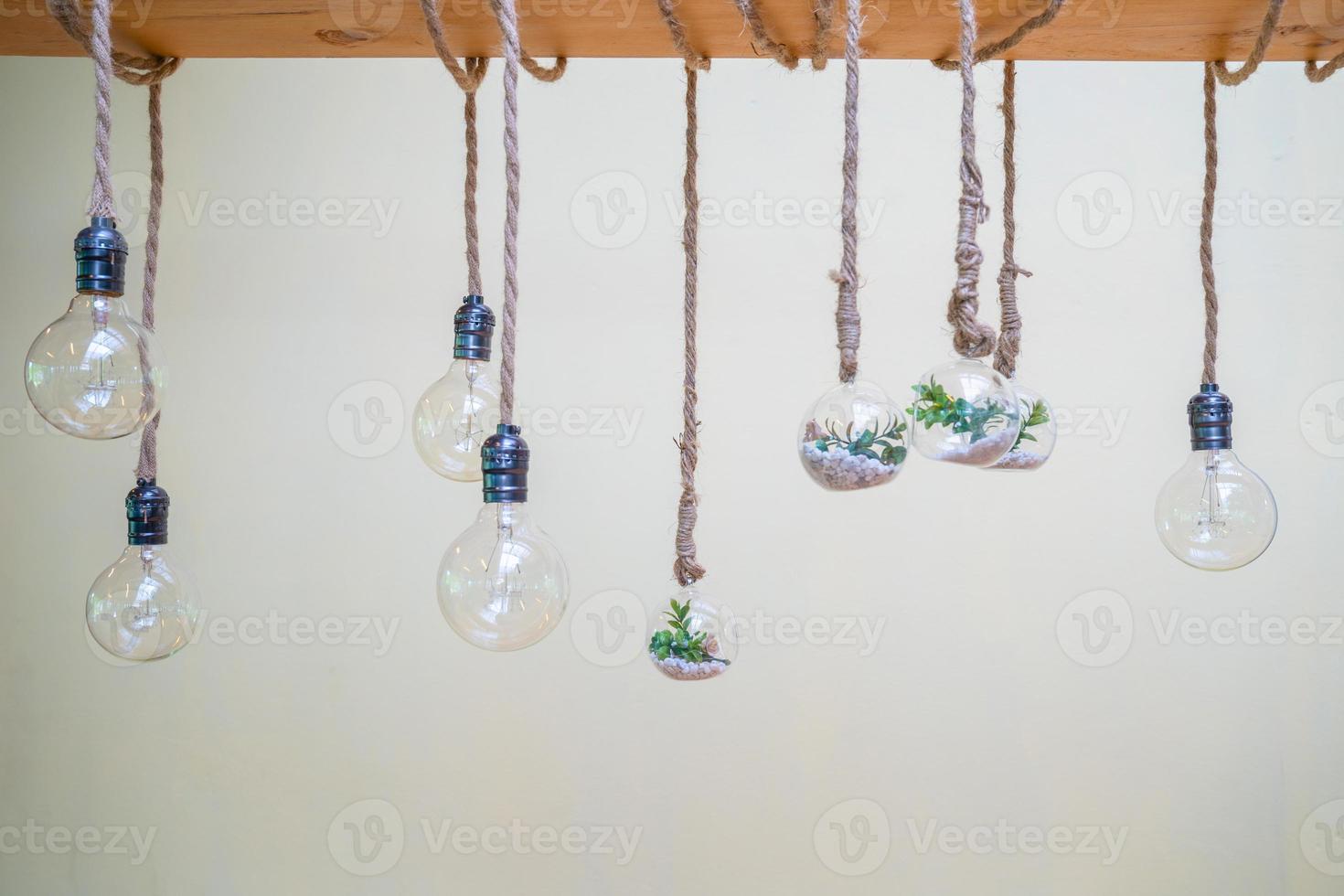 Decorated cozy lamps stick in the rope and little tiny tree with small white rock inside the ball glass hang on to big wood log in front of white background. photo