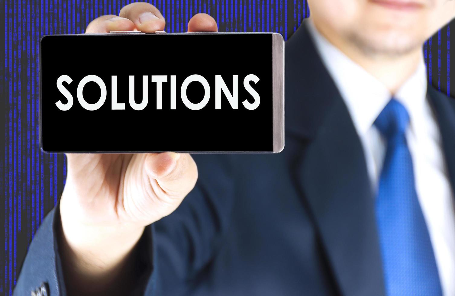 SOLUTIONS word on mobile phone screen in blurred young businessman hand and digital technology background, business concept photo