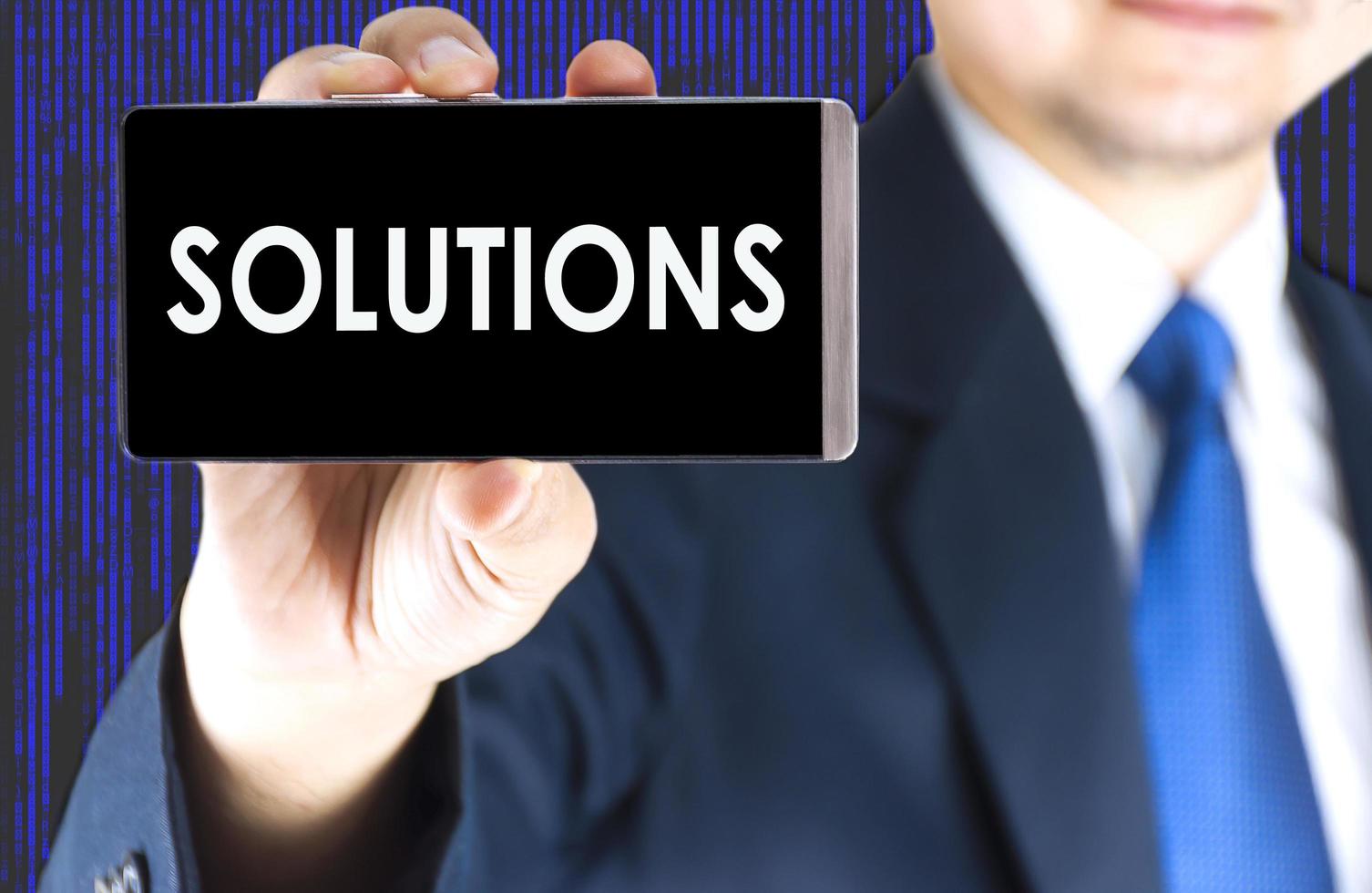 SOLUTIONS word on mobile phone screen in blurred young businessman hand and digital technology background, business concept photo