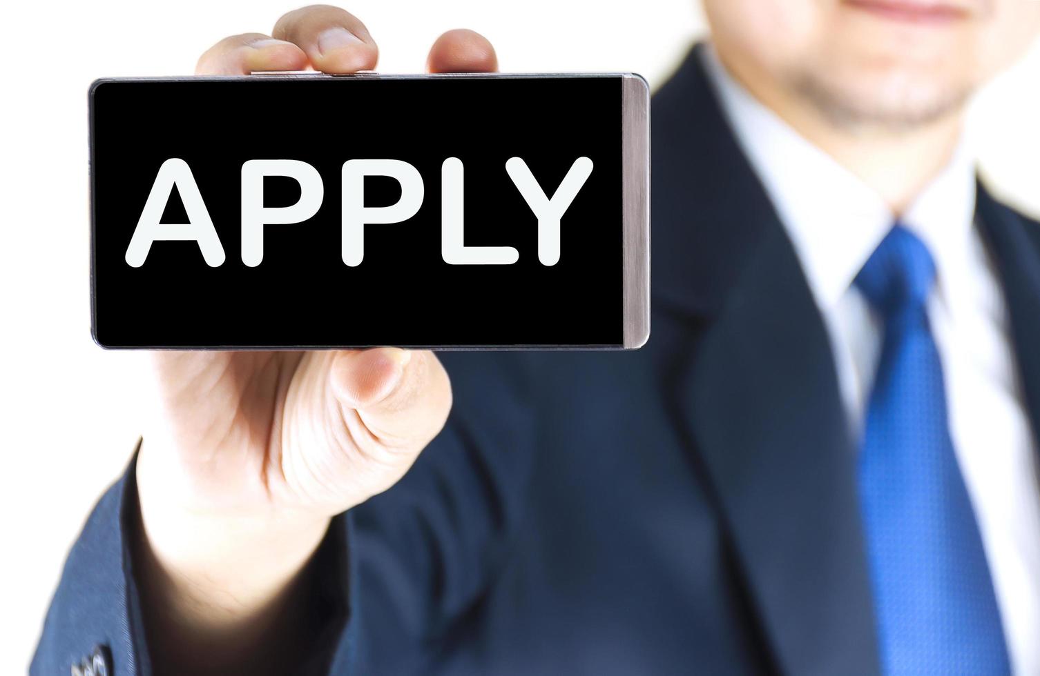 APPLY, word on mobile phone screen in blurred young businessman hand over white background, business concept photo