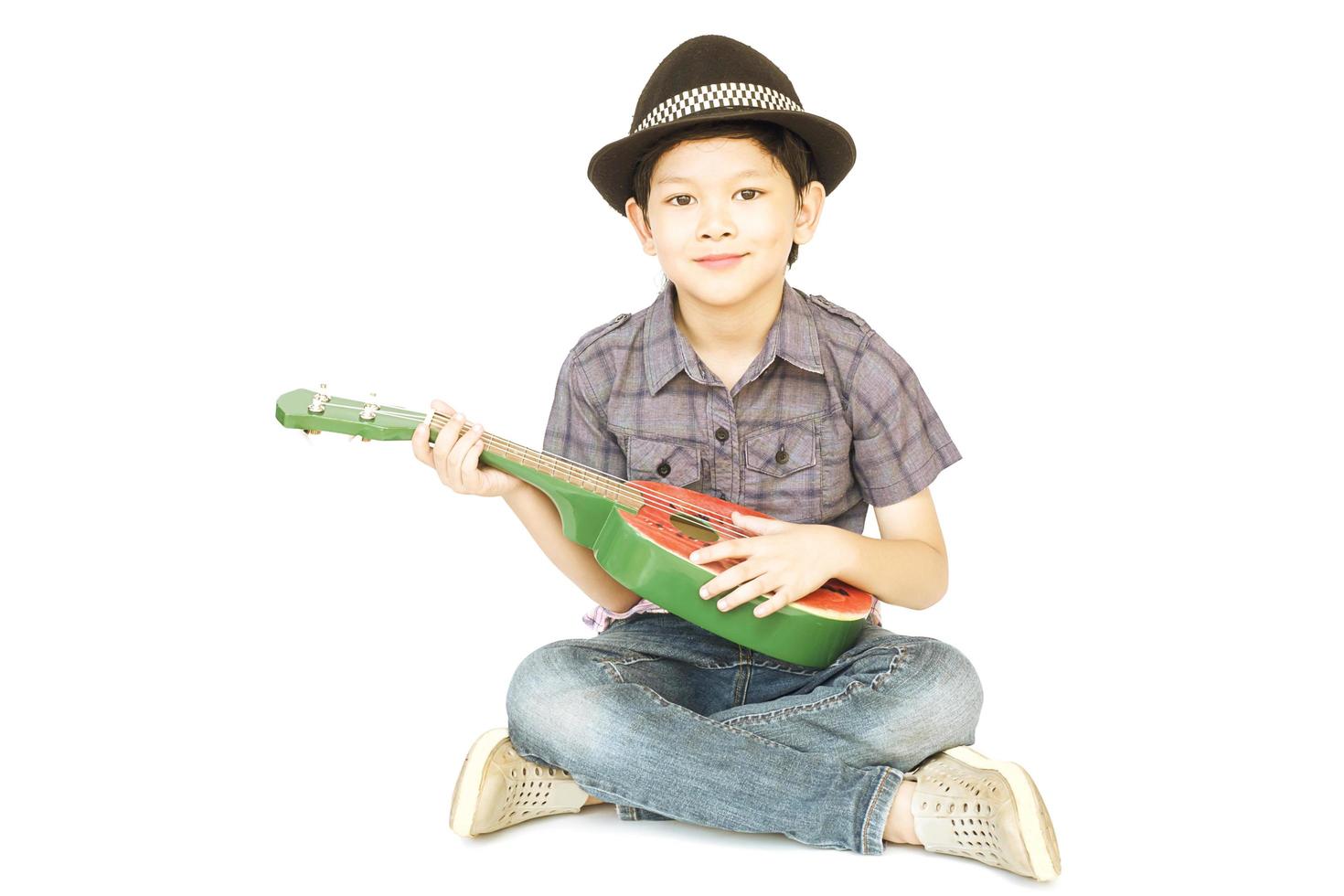 Vintage photo of 7 years old Asian boy is sitting and playing ukulele isolated over white.