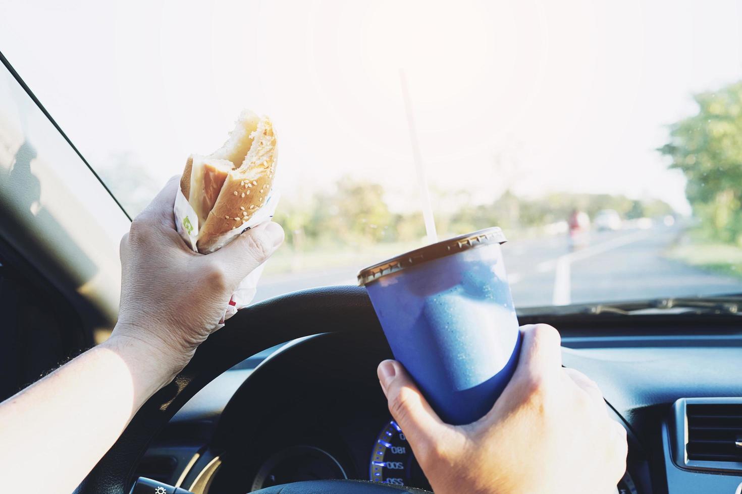 Man is dangerously eating hot dog and cold drink while driving a car photo