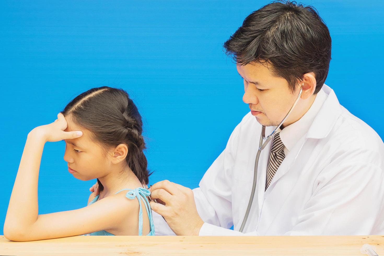 Sick Asian girl is being treated by male doctor over blue background photo