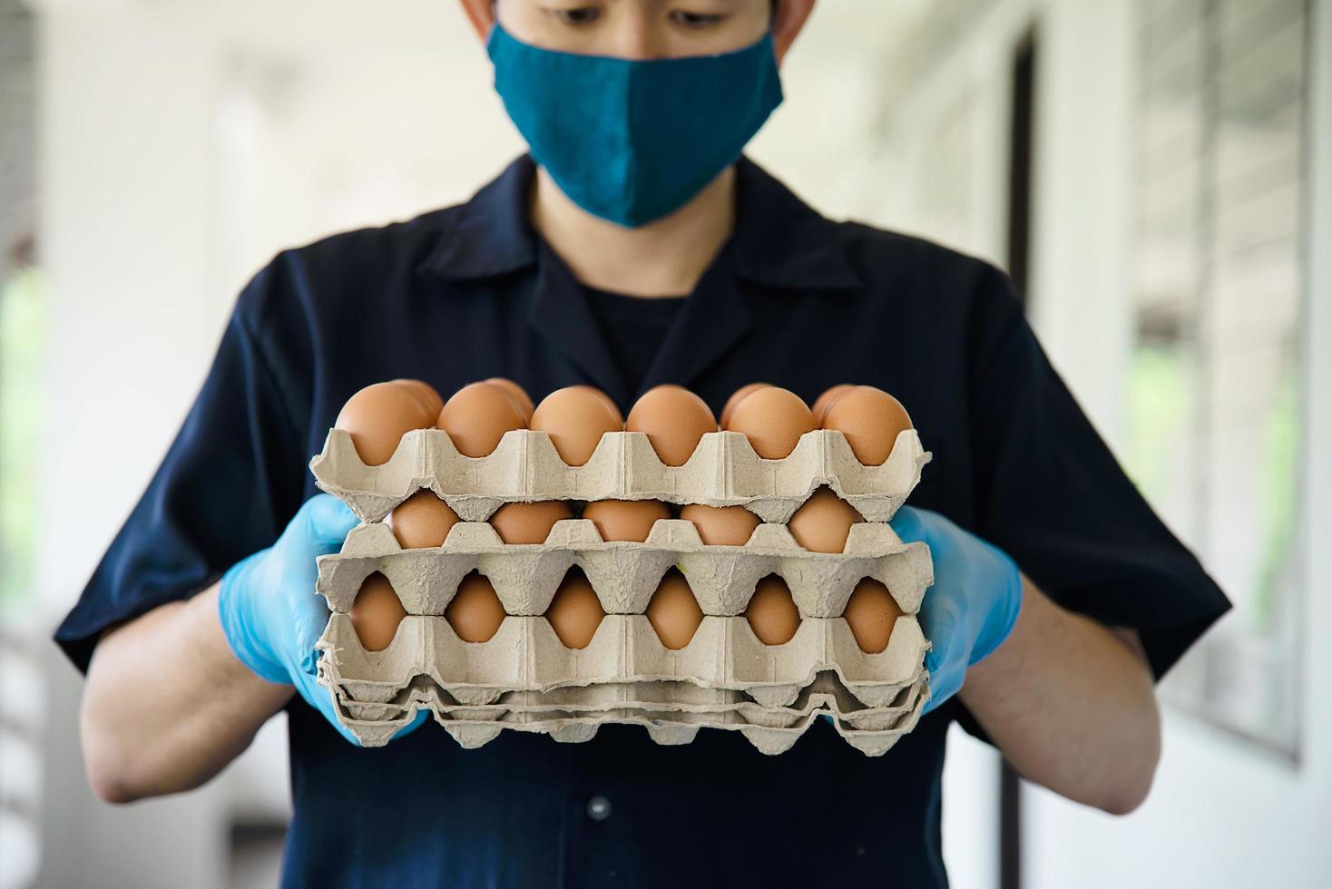 A man carry 3 layers eggs tray for stay safe at home putting sanitary glove during corona virus COVID-19 spreading - people keeping food in COVID-19 viral spread period concept. photo