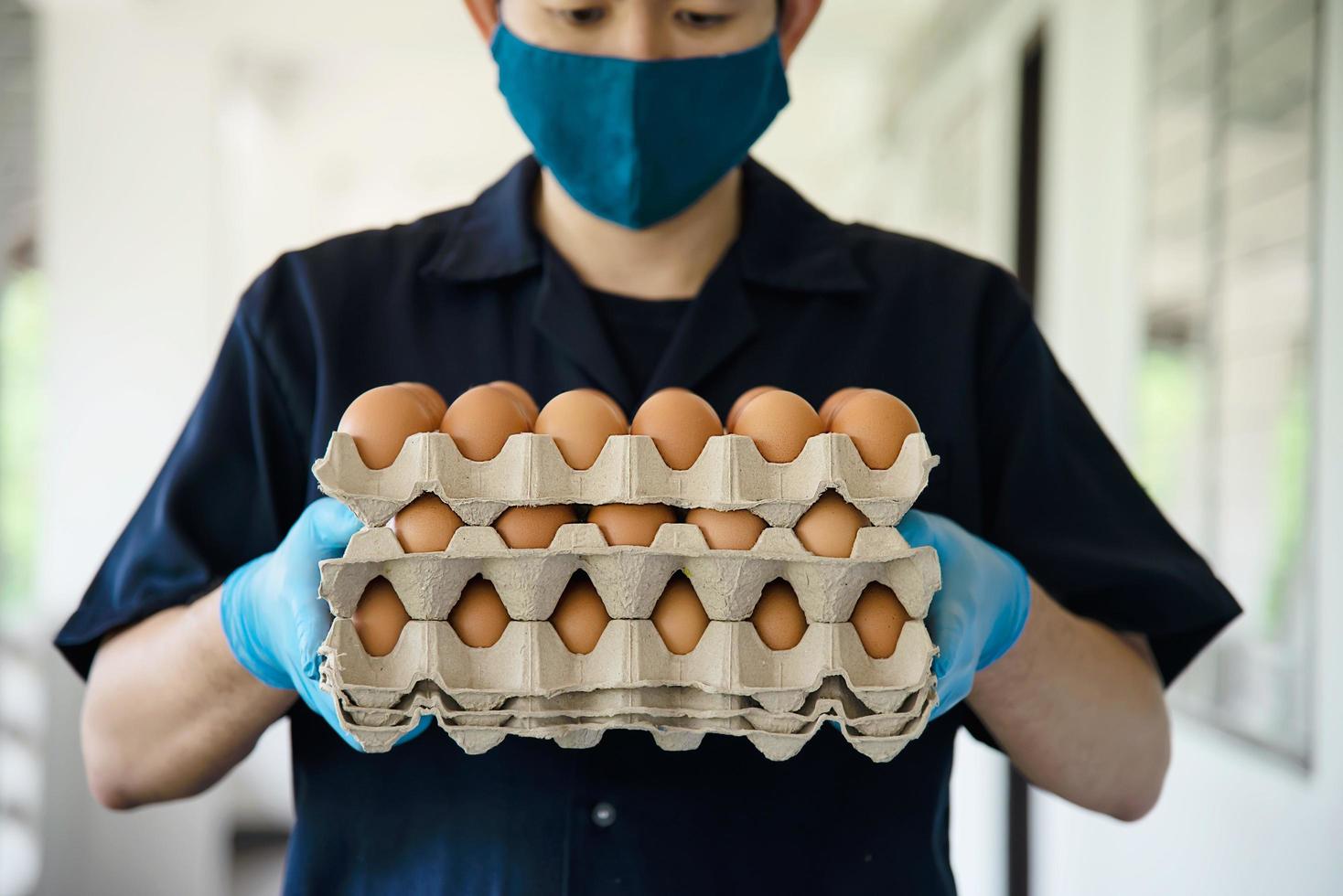 un hombre lleva una bandeja de huevos de 3 capas para mantenerse seguro en casa poniendo guantes sanitarios durante la propagación del virus corona covid-19 - personas que mantienen alimentos en el concepto de período de propagación viral covid-19. foto