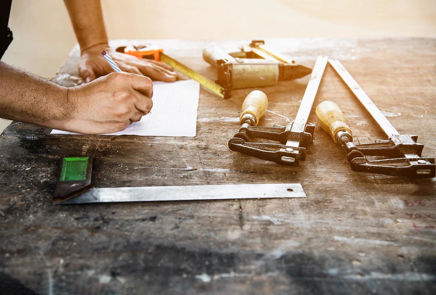 Carpenter working with wood furniture product preparation using hand tools and machine table station while writing paper photo