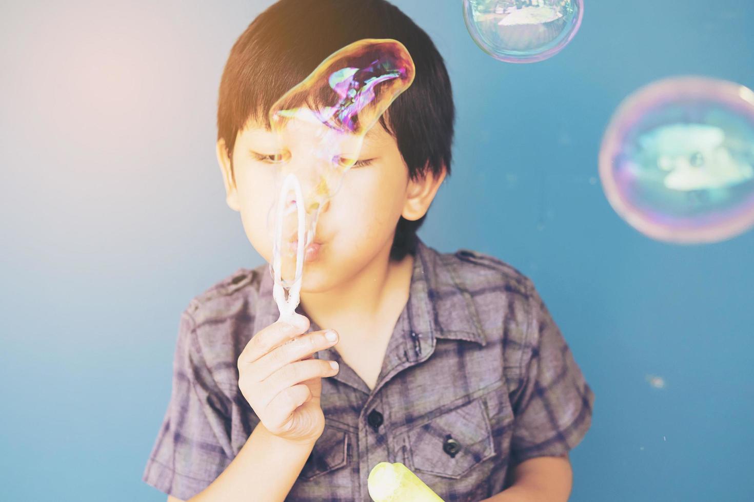 Asian boy is blowing bubble over light blue background photo