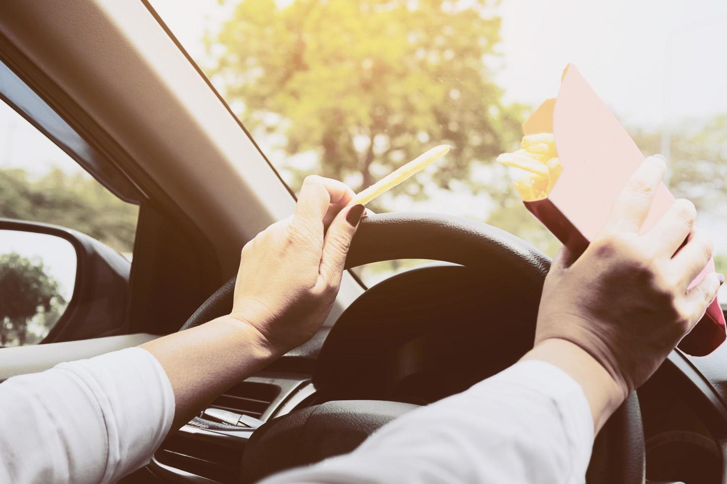 Lady eating french fries white driving car dangerously photo