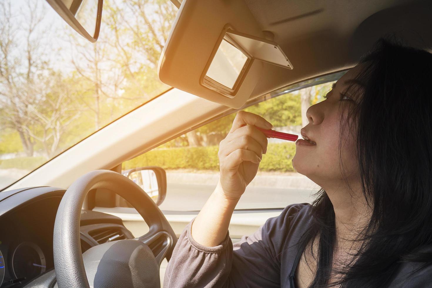 Woman making up her face using lipstick while driving car, unsafe behavior photo