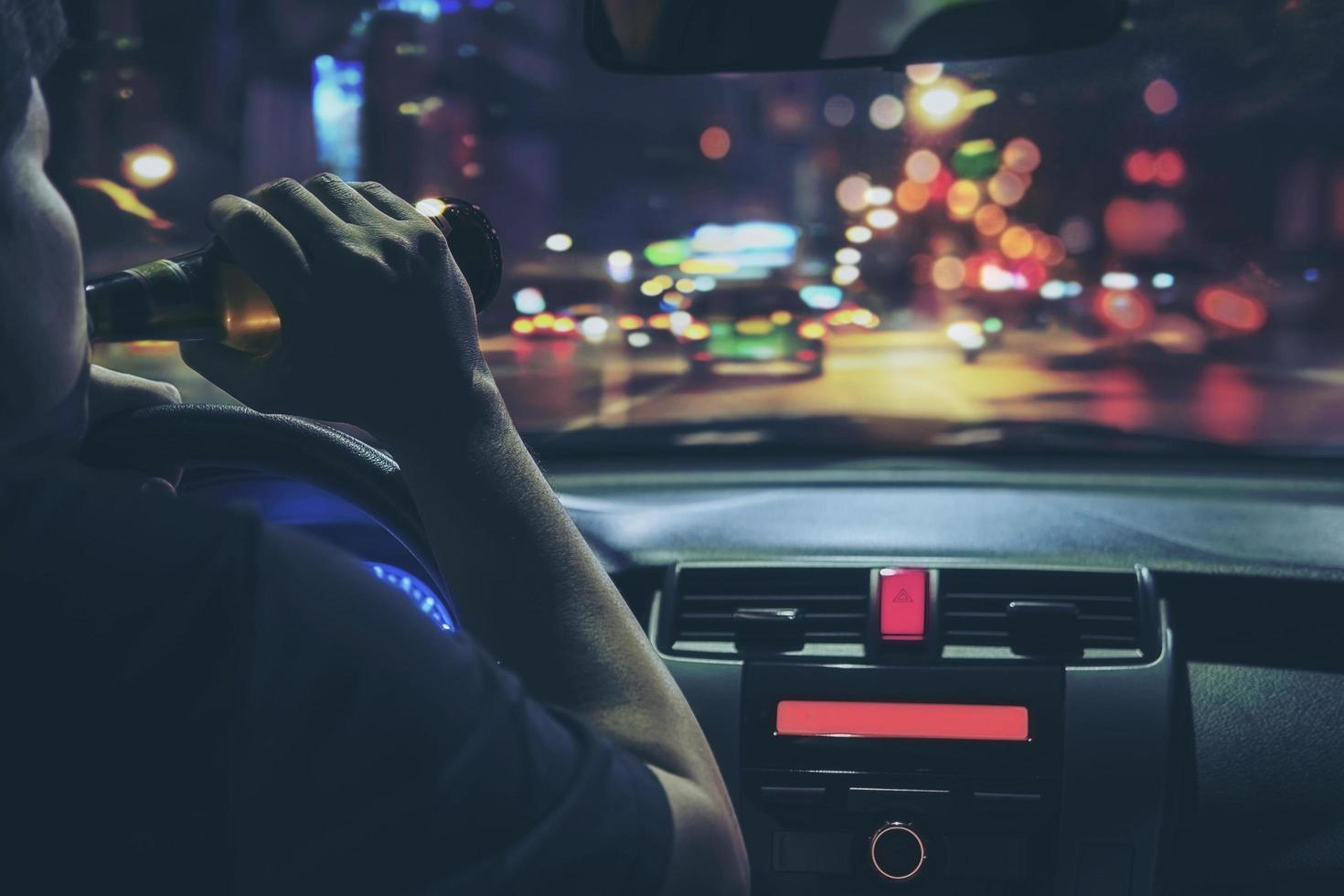 Man drink beer while driving at night in the city dangerously, left hand drive system photo