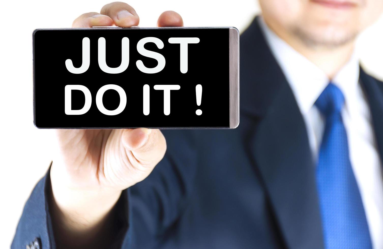 JUST DO IT  word on mobile phone screen in blurred young businessman hand over white background, business concept photo