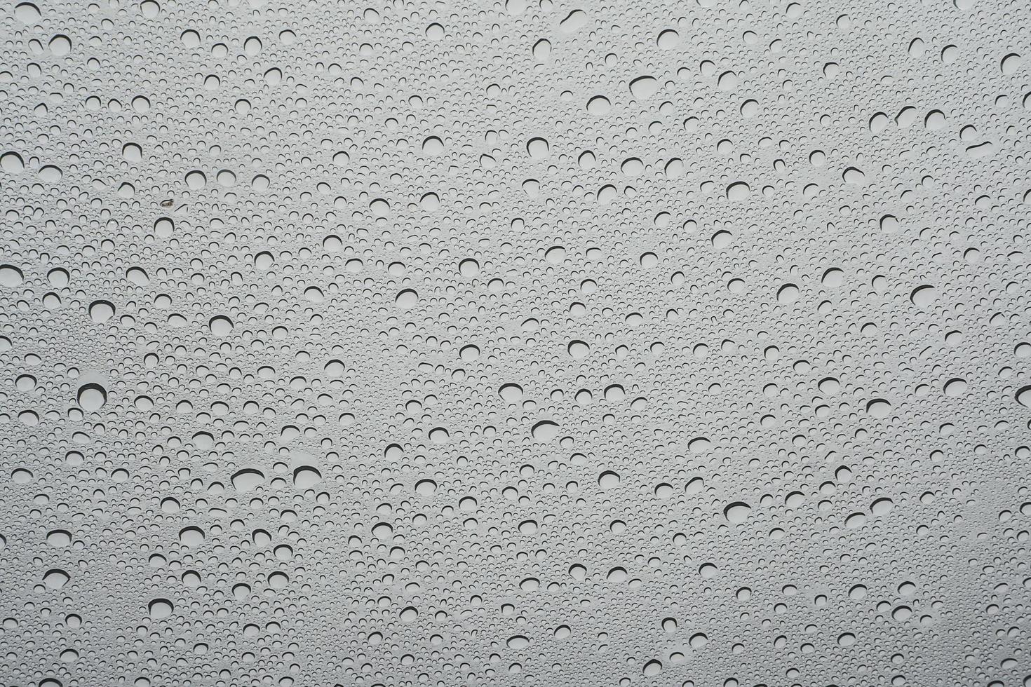 Rain drop on at glass window over gray sky background photo