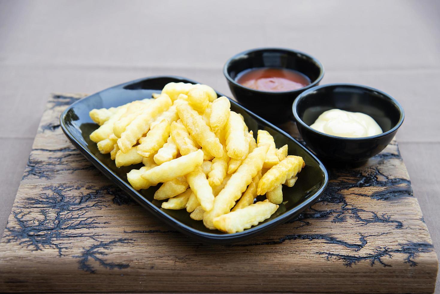 Side view of French fries with sauces on wood plate photo