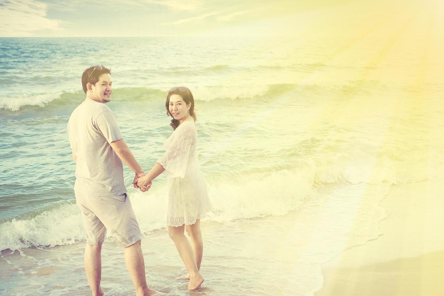 Vintage tone photo of Asian couple on beach with warm sun light from top corner