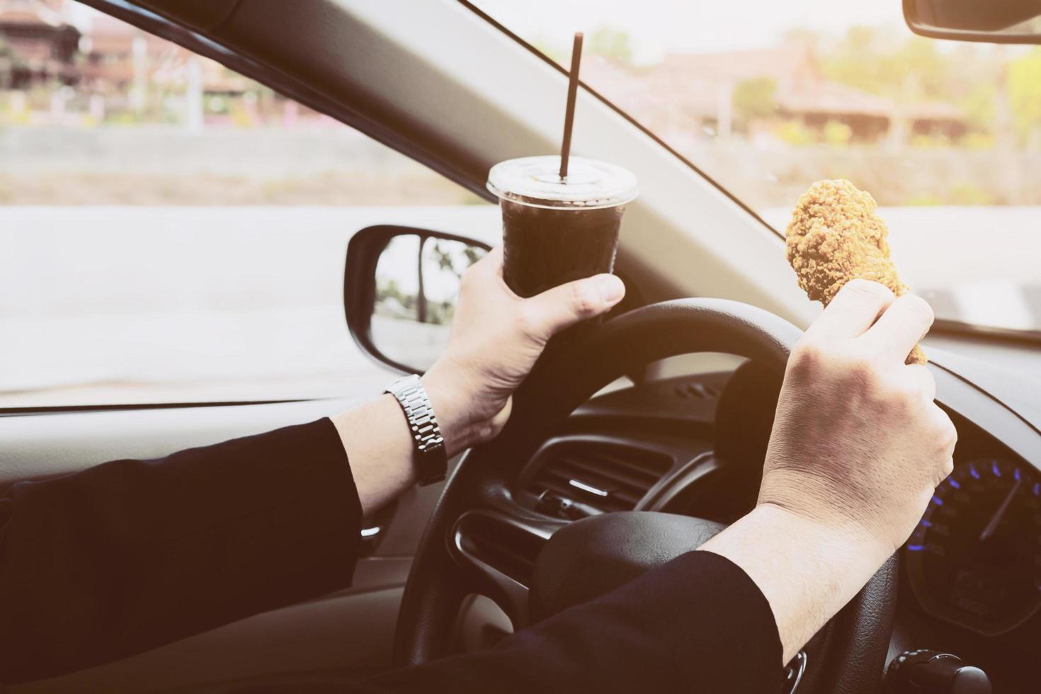 hombre de negocios conduciendo un coche mientras come pollo frito y refrescos fríos peligrosamente foto