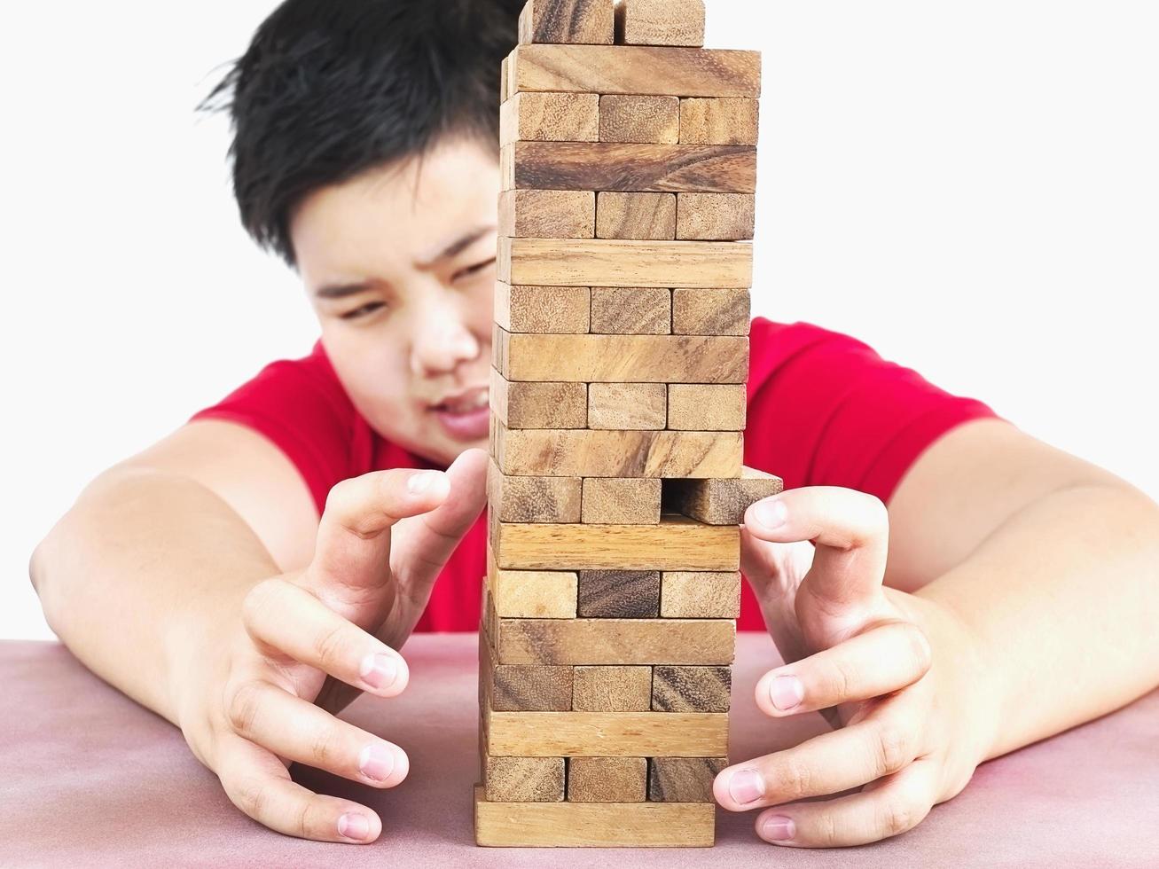 un niño asiático está jugando un juego de torre de bloques de madera para practicar habilidades físicas y mentales. la foto se centra en las manos del modelo y se aísla en blanco.