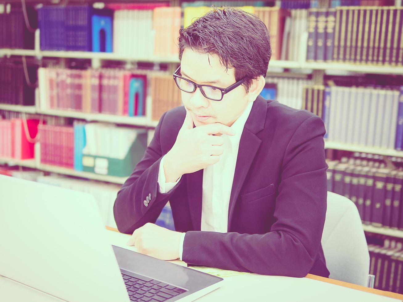 Vintage style photo of a man is working with laptop computer in his office. Photo is focused at his face.