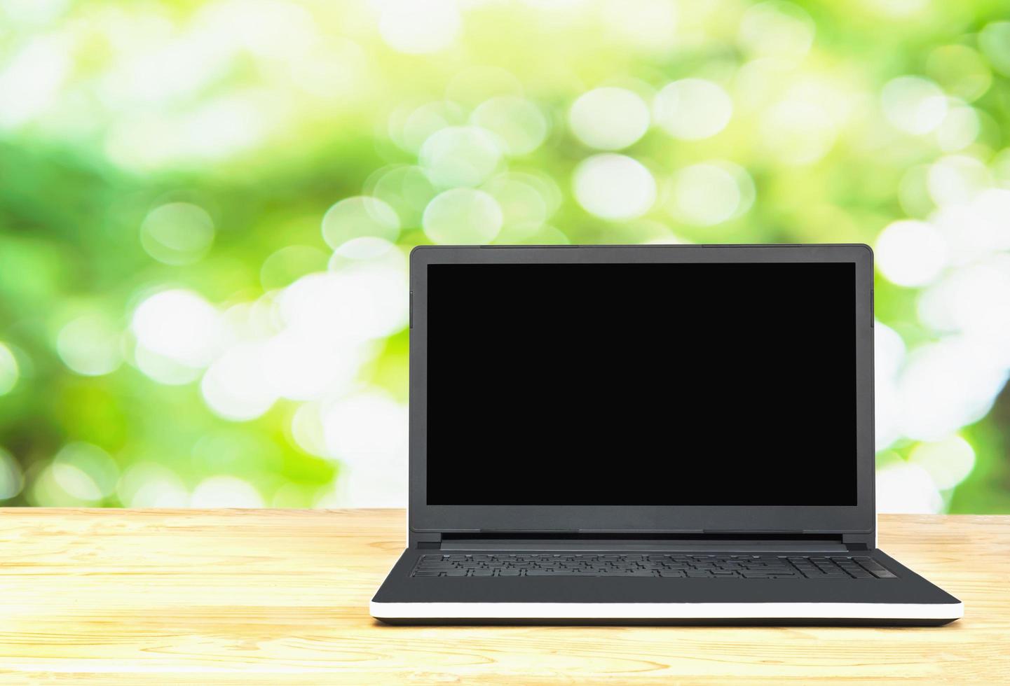 Laptop on table top over green tree with white bokeh natural background. Photo includes CLIPPING PATH of blank screen.